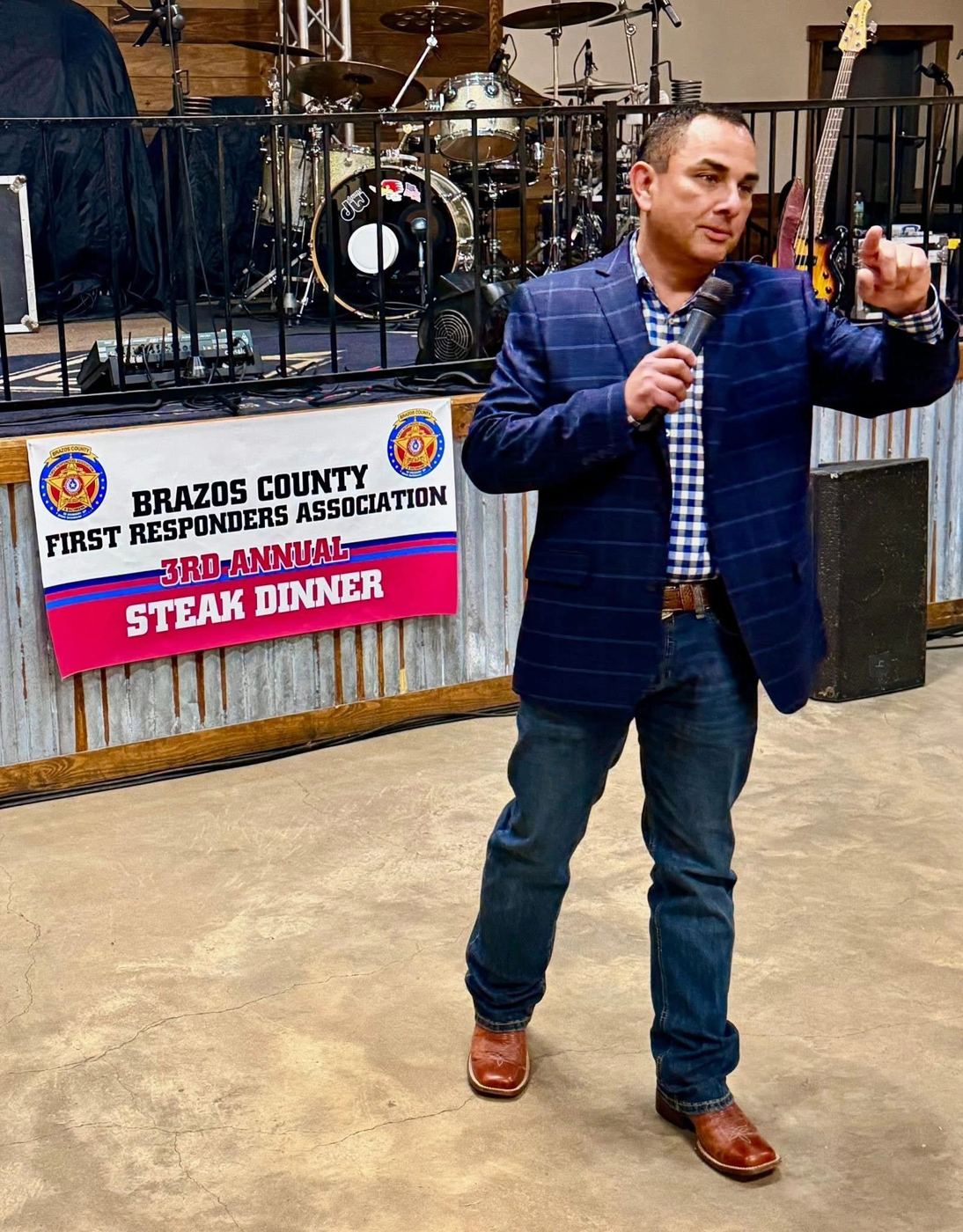 Speaker addressing the crowd beside the 3rd Annual Steak Dinner banner